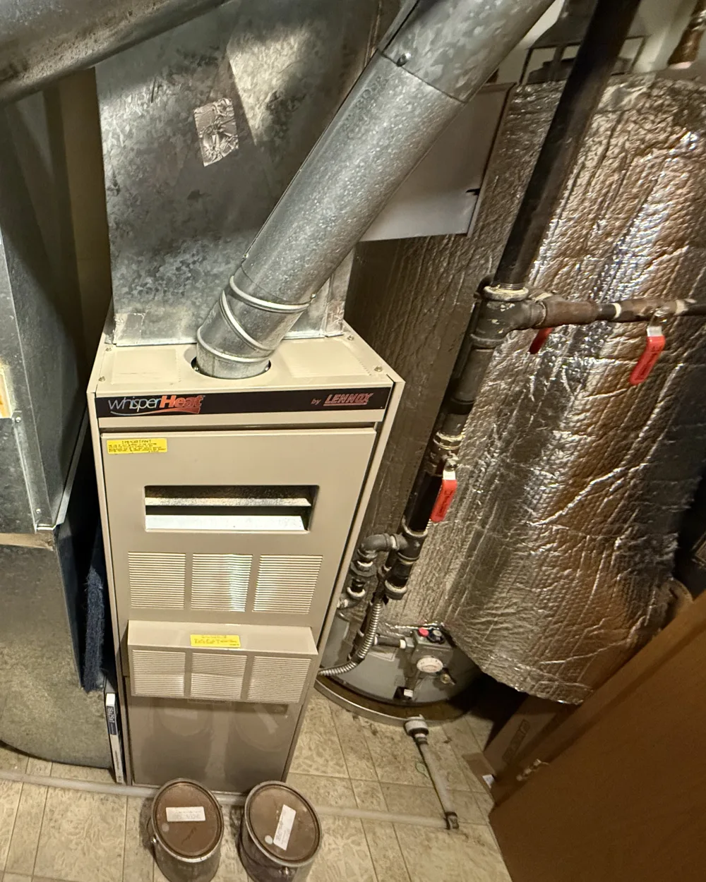 Older hot water tank wrapped in insulation beside an aging furnace, before replacement